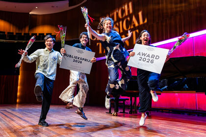Vier gelukkige artiesten springen op een podium, elk met een bloempot en een bord met "Award 2023".