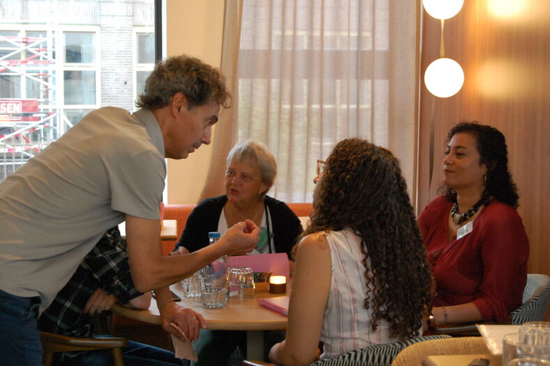 Een groep mensen in gesprek tijdens een bijeenkomst, met een focus op de spreker aan de voorkant.