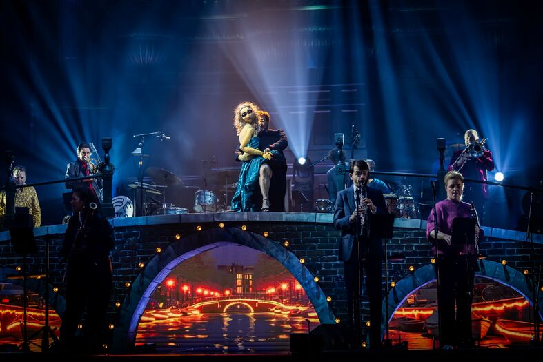 Een energieke muzikale voorstelling op een podium met dansers en bandleden, onderstreept door sfeervolle verlichting.