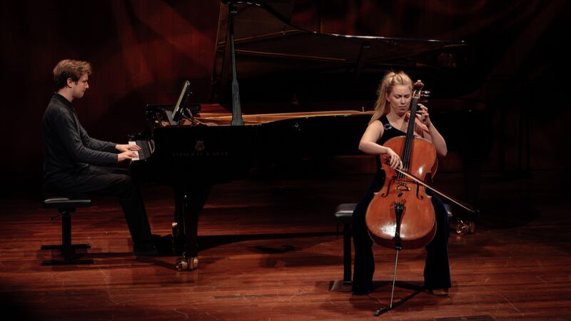 Een cellist en pianist spelen samen op een podium voor een publiek.