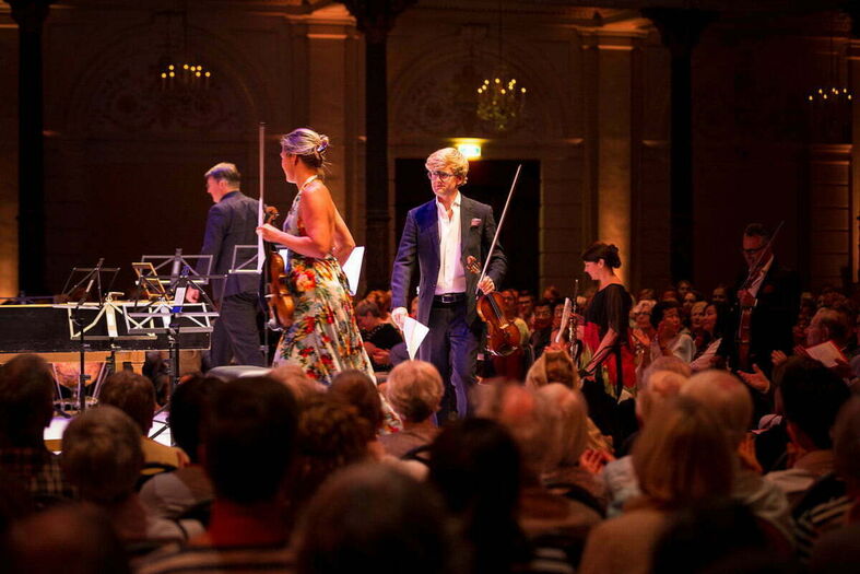 Concertzaal met muzikanten met instrumenten, publiek in elegante kleding, en een sfeer van een live uitvoering.