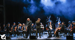 Een orkest op een podium met muzikanten in klassieke kleding, klaar om te beginnen met spelen.
