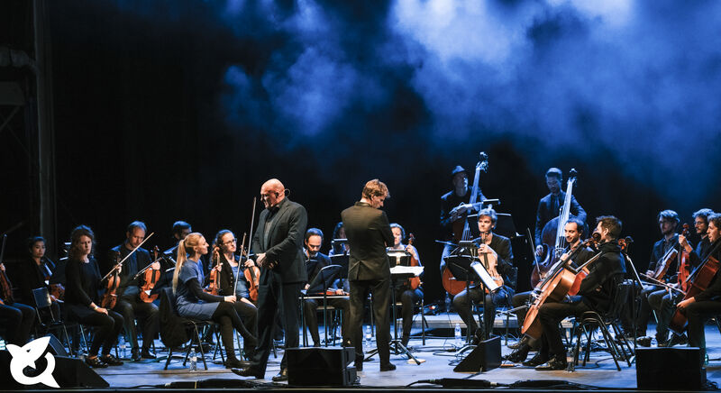 Een orkest op een podium met muzikanten in klassieke kleding, klaar om te beginnen met spelen.