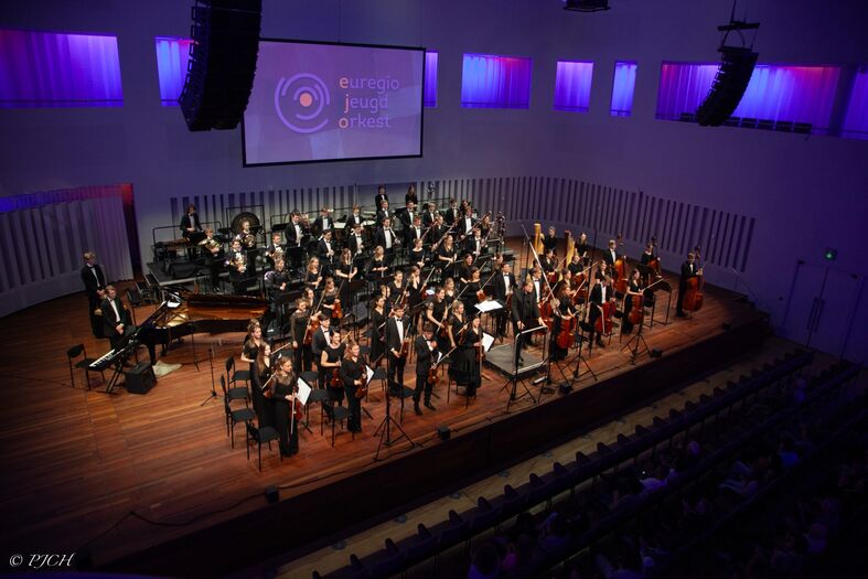 Een symfonieorkest speelt op een podium in een moderne concertzaal met sfeervolle verlichting.