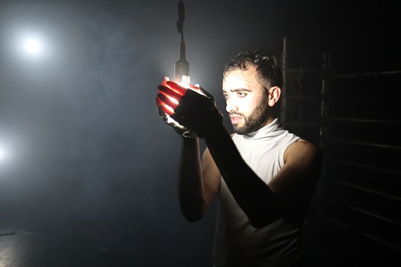 Man in een lichte shirt houdt een rode lamp vast, omgeven door een mistige en schimmige omgeving met zachte verlichting.