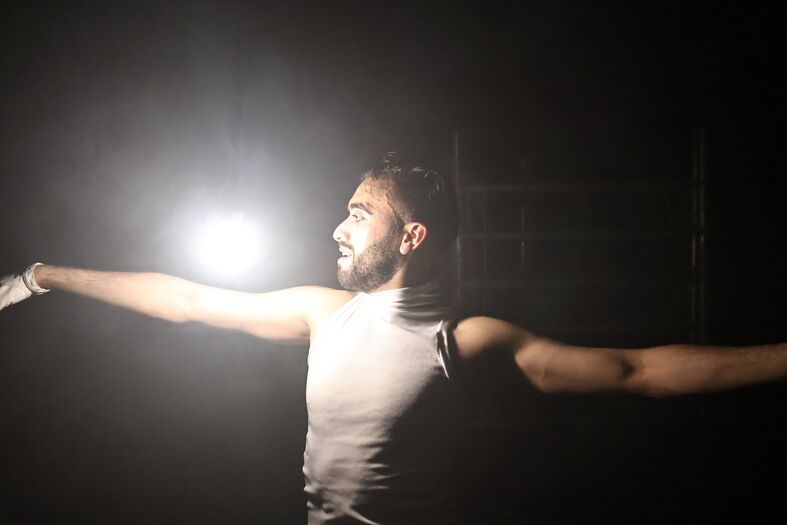 Een man met uitgestrekte armen staat in een donkere ruimte, verlicht door een felle lichtstraal.