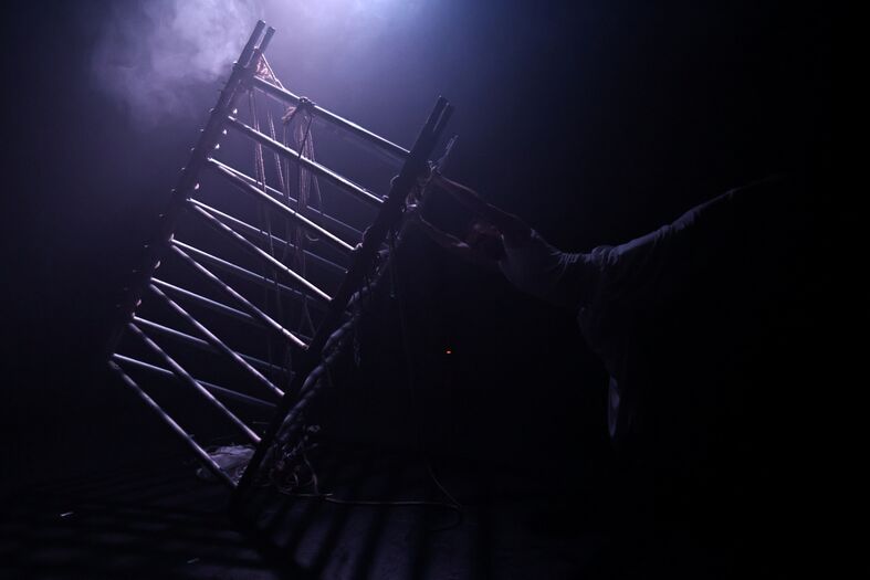 Een silhouet van een persoon die acrobatische bewegingen maakt op een ladder, verlicht door een zachte lichtbron.