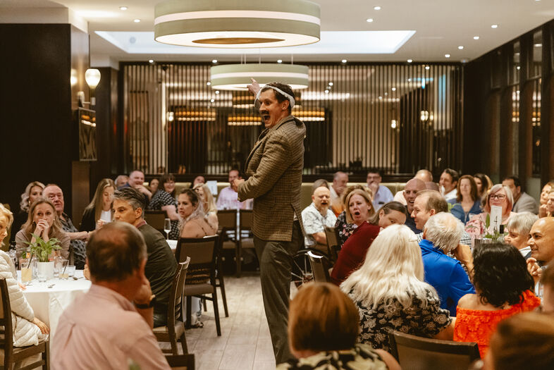 Een sprekende man staat in een restaurant voor een aandachtig publiek tijdens een evenement of diner.
