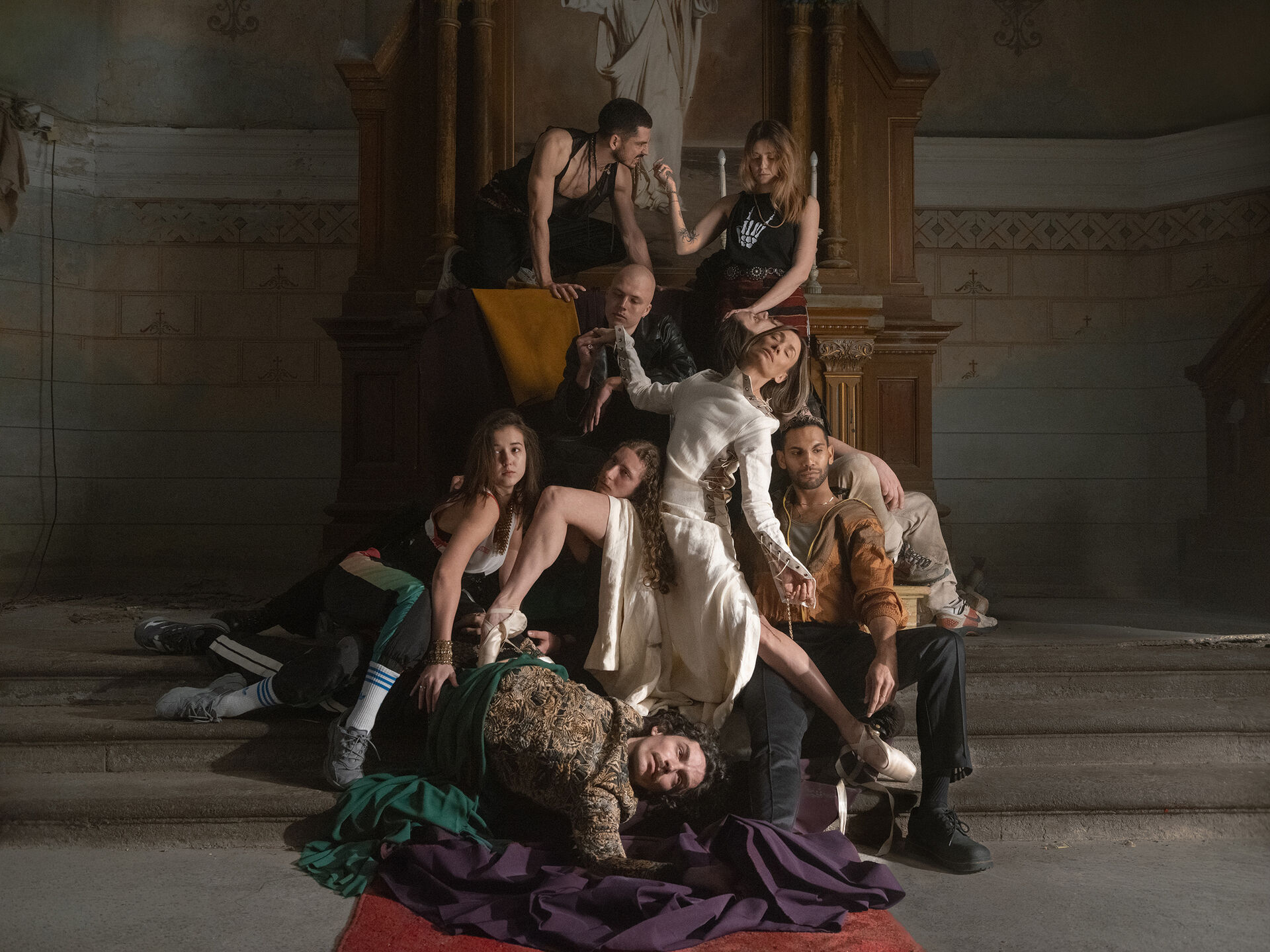 Groep performers ligt en zit gestapeld op stenen trappen in historische ruimte.