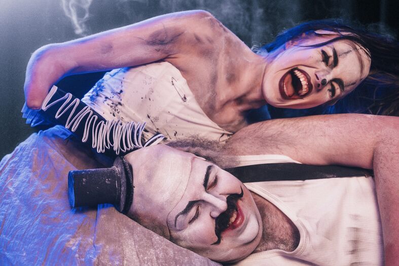 Een kunstenaar en performer in een theatrale voorstelling, met opvallende make-up en kostuums, in een dramatische pose.