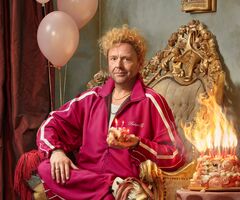 Richard Groenendijk in roze trainingspak zit op sierlijke stoel naast brandende taart en ballonnen