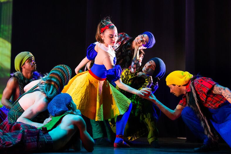 Dansers in kleurrijke kostuums voeren een scène op met een personage dat lijkt op Sneeuwwitje.