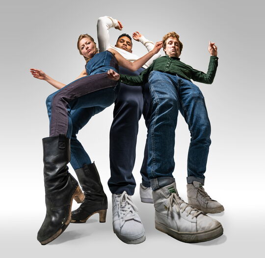 Drie mensen in verschillende outfits staan met uitgespreide benen, elk met unieke schoenen op een neutrale achtergrond.