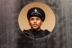 Een man in een politie-uniform kijkt door een ronde opening in een houten paneel.