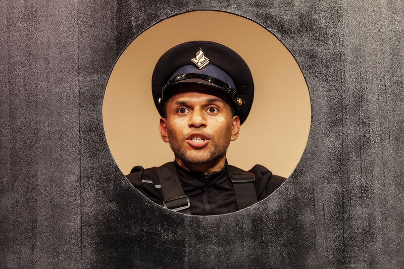 Een man in een politie-uniform kijkt door een ronde opening in een houten paneel.
