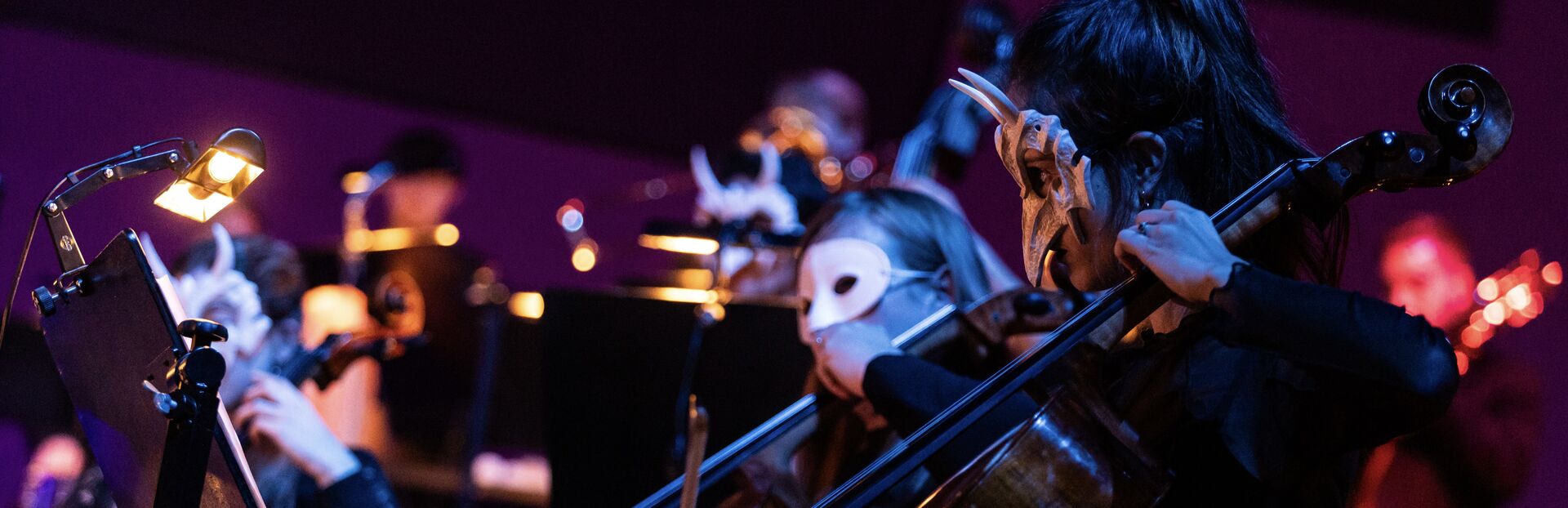 Musici spelen samen op een podium, met focus op een cellist en andere orkestleden op de achtergrond.