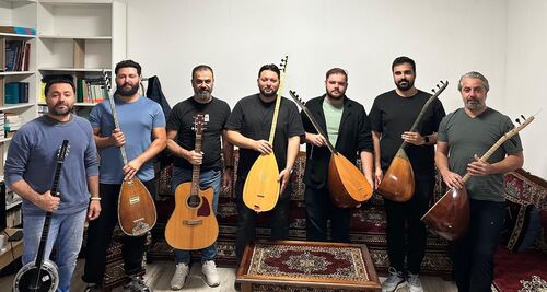 Groep van acht muzikanten met verschillende instrumenten staand voor een boekenkast en een groot tapijt.