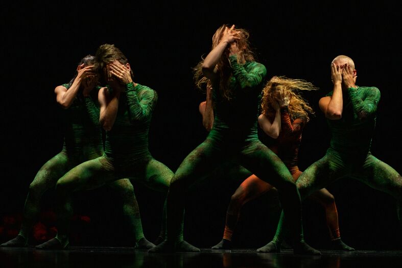 Vijf dansers in groene outfits voeren een energieke choreografie uit op een donkere achtergrond.