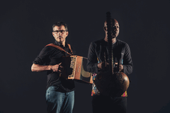 Twee muzikanten staan zij aan zij, één met een accordeon en de ander met een Afrikaanse snaarinstrument.