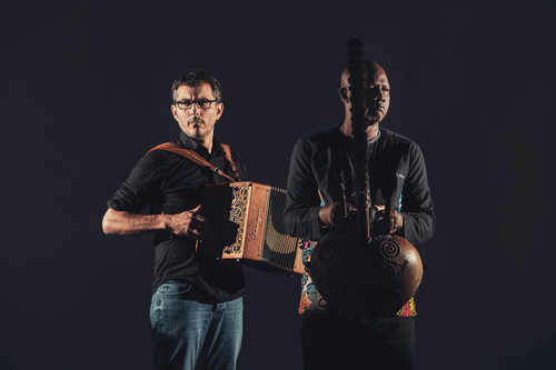 Twee muzikanten staan zij aan zij, één met een accordeon en de ander met een Afrikaanse snaarinstrument.