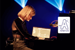 Een muzikante speelt piano op een podium met verlichting op de achtergrond.