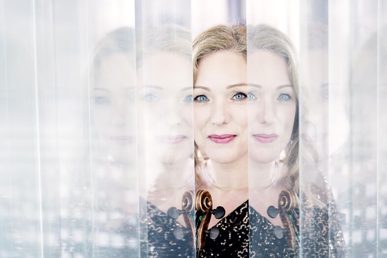 Een vrouw staat in een reflecterende omgeving met een mysterieuze uitstraling, gefocust en zonder glimlach.
