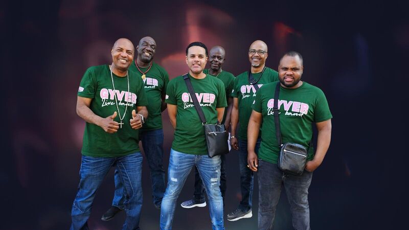 Zes mensen in groene T-shirts poseren samen voor een achtergrond met een vage, kleurrijke uitstraling.