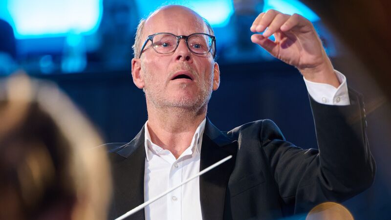 Dirigent Jacco Nefs in smoking leidt een orkest, met een focus op zijn handbeweging en een oordeelloze blik.