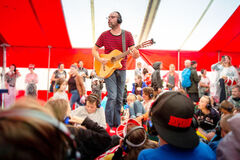Muzikant met gitaar speelt voor een enthousiast publiek in een tent, terwijl bezoekers met koptelefoons luisteren.