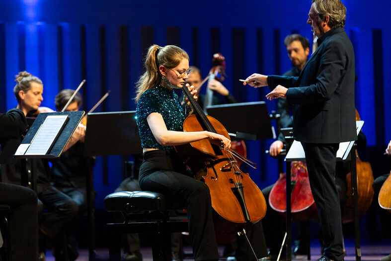 Een celliste speelt in een orkest tijdens een live optreden, onder toezicht van de dirigent.