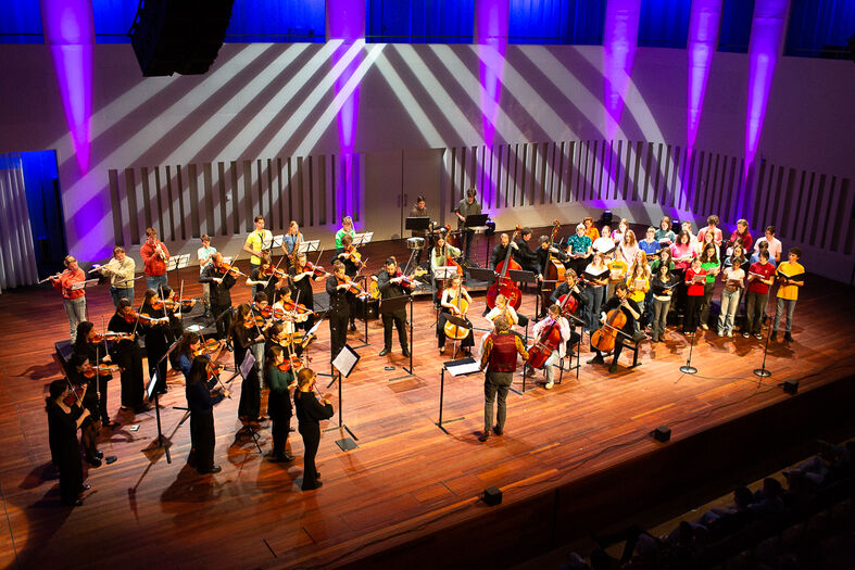 Een orkest met diverse muzikanten speelt op een podium met kleurrijke verlichting.