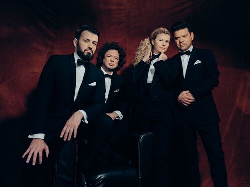Vier mensen in tuxedo's poseren serieus voor een rode achtergrond, met een mix van krachtige en elegante houdingen.