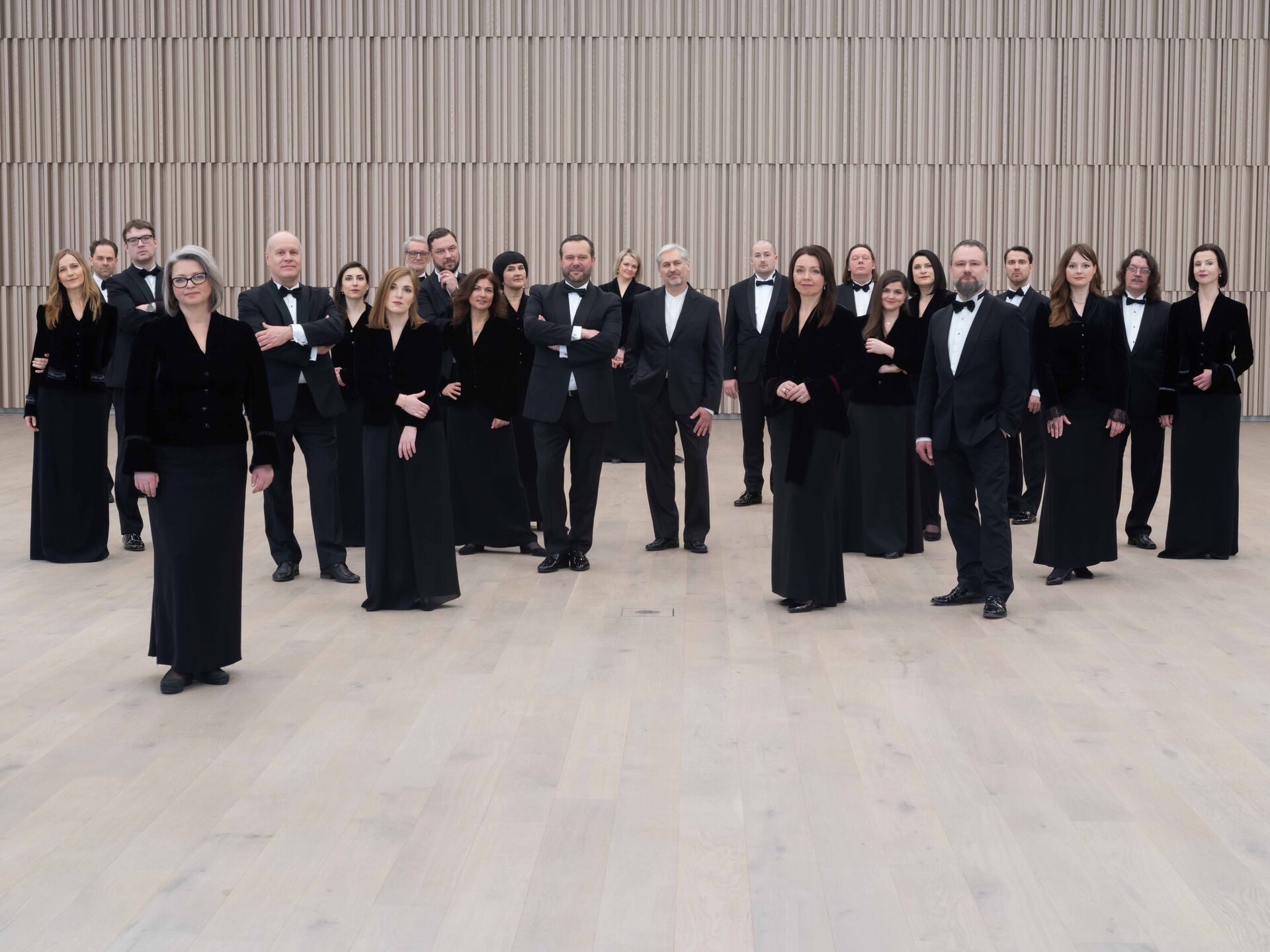 Groepsportret van een symfonieorkest, gekleed in formele zwarte kleding, staand in een moderne concerthal.
