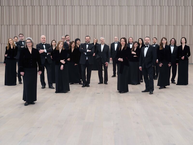 Groepsportret van een symfonieorkest, gekleed in formele zwarte kleding, staand in een moderne concerthal.