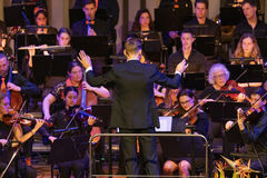 Een dirigent leidt een orkest tijdens een optreden, met muzikanten die verschillende instrumenten bespelen.