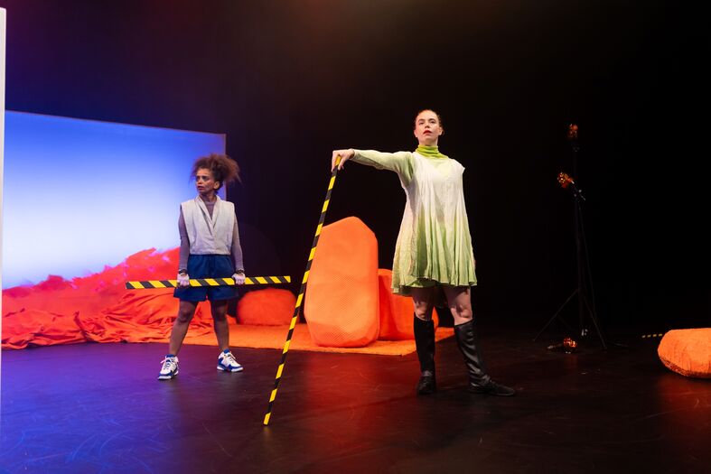 Twee performers posteren met afzetbalken op een podium met felgekleurde oranje objecten.