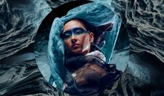 Persoon met blauwe oogmake-up, omhuld door doorschijnende stoffen binnen ronde kadering tegen waterachtig decor.