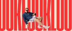 Luuk Weggemans ligt nonchalant achterover op een witte stoel, gekleed in een donker overhemd, gestreepte shorts en witte sokken, voor een achtergrond met grote rode letters.