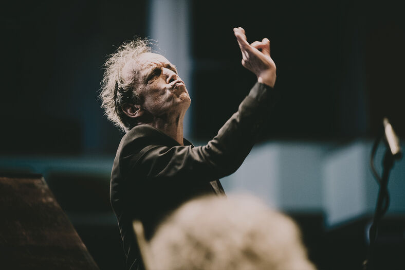 Dirigent leidt een orkest met expressieve gebaren, gefotografeerd vanuit een lage hoek.