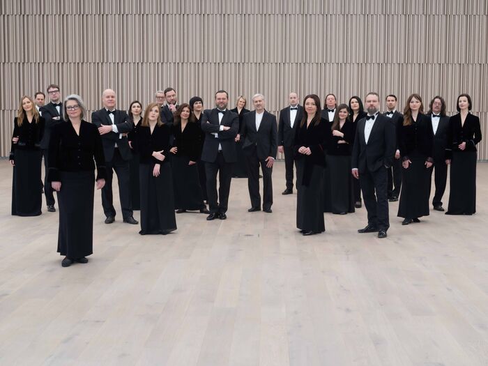 Groepsportret van een symfonieorkest, gekleed in formele zwarte kleding, staand in een moderne concerthal.