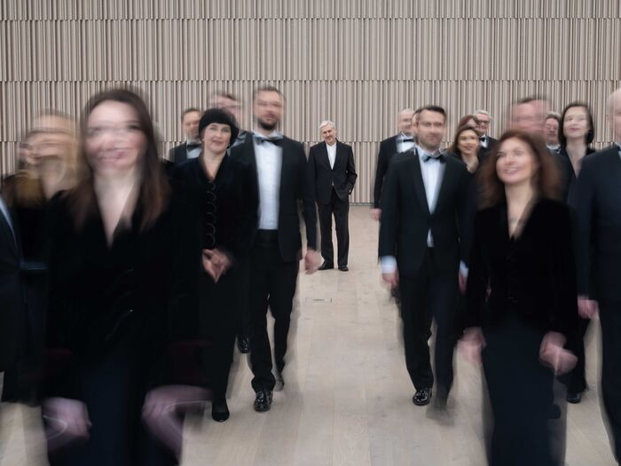 Groep mensen in formele kleding loopt samen naar de camera in een moderne binnenruimte. Achtergrond is onscherp.