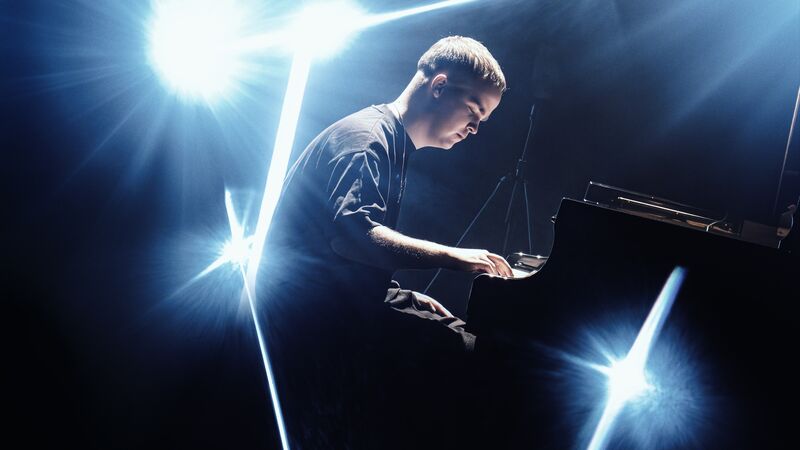 LEVI.SCT speelt een zwart steinway piano onder heldere verlichting op een podium.