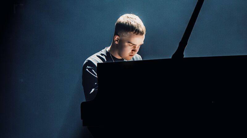 LEVI.SCT speelt piano op een podium, met focus op zijn spel in een sfeervolle, lichtblauwe achtergrond.