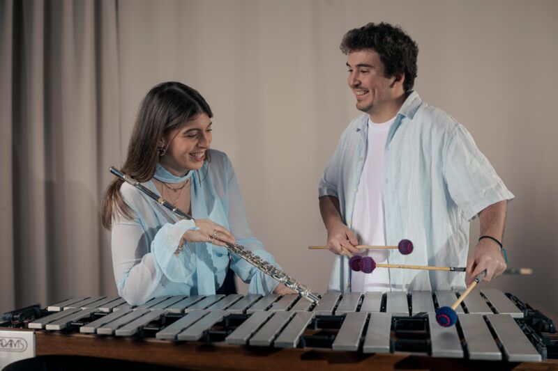 Twee muzikanten spelen samen op een marimba, met een fluit en mallets in de handen.