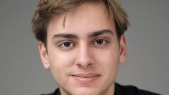 Portret van een jonge man met blond haar, in een zwart shirt, tegen een neutrale achtergrond.