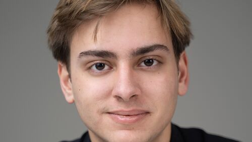 Portret van een jonge man met blond haar, in een zwart shirt, tegen een neutrale achtergrond.