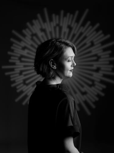 Portret van een vrouw in profiel, tegen een dramatische, stralende achtergrond in zwart-wit.