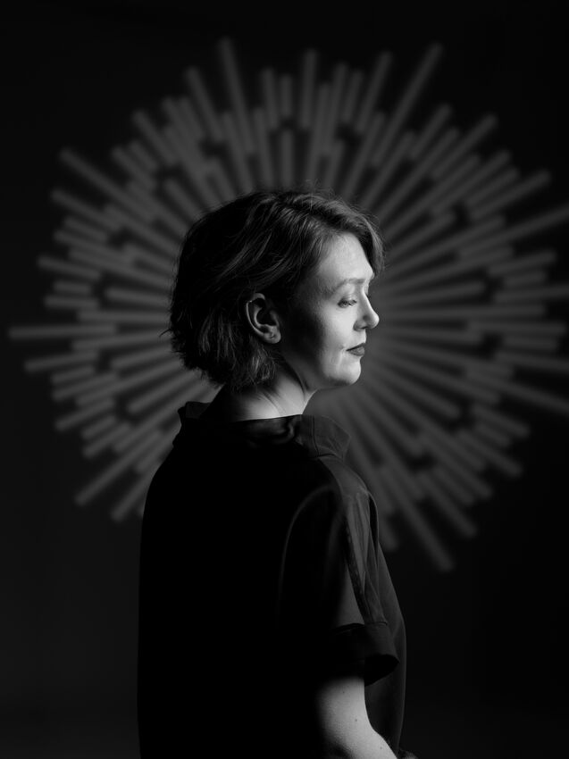Portret van een vrouw in profiel, tegen een dramatische, stralende achtergrond in zwart-wit.