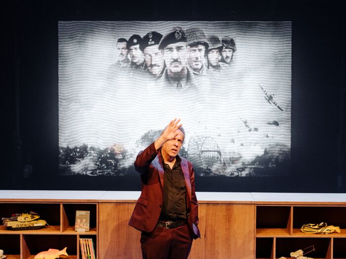 Marcel van Roosmalen in een pak staat op het podium met een achtergrond van historische figuren en een oorlogsscène.
