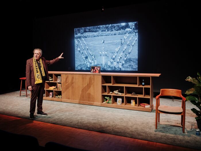 Marcel van Roosmalen toont een afbeelding op een scherm tijdens een presentatie op een podium met een minimalistische inrichting.